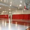 Indoor gym with a basketball hoop on the right and red privacy curtains along the walls.