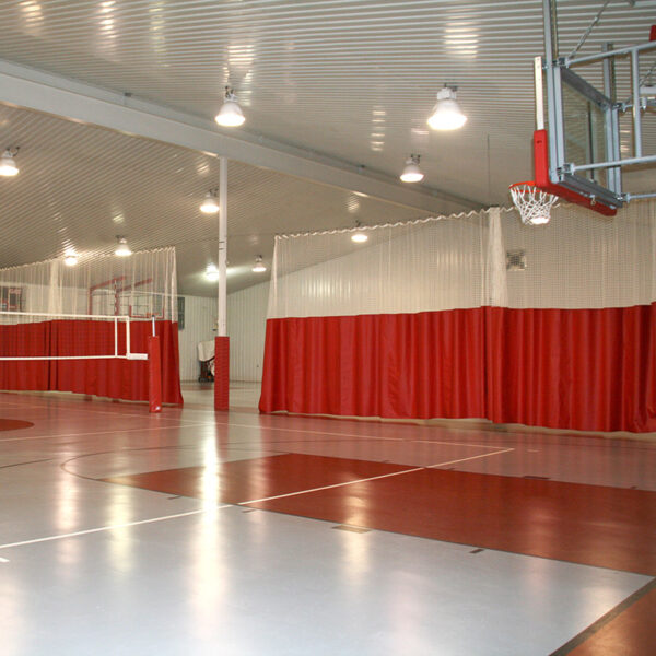 Indoor gym with a basketball hoop on the right and red privacy curtains along the walls.