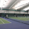 Indoor tennis facility with four players on a doubles court near the net.