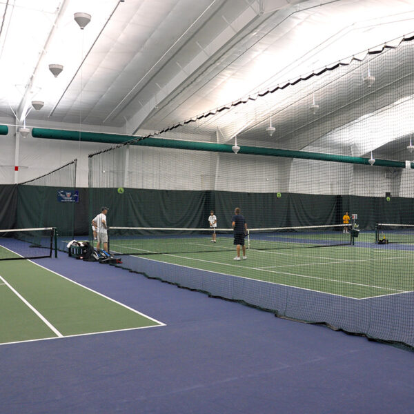Indoor tennis facility with four players on a doubles court near the net.