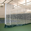 Indoor sports facility with a white net enclosure around a court or practice area; padded base along the bottom of the netting.