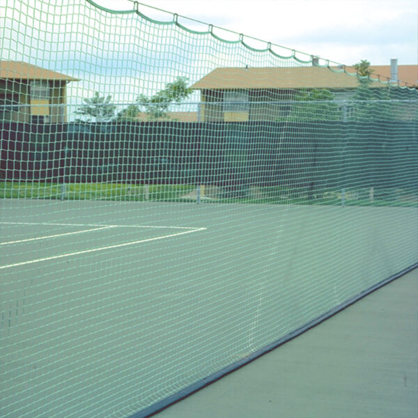 Outdoor tennis court with green mesh fence and netting, buildings in the background.