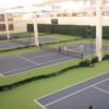 Two young players stand near the net on an indoor tennis court, with other courts and green padded walls in the background.