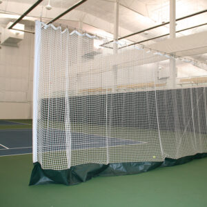 Indoor sports facility with a white net enclosure around a court or practice area; padded base along the bottom of the netting.