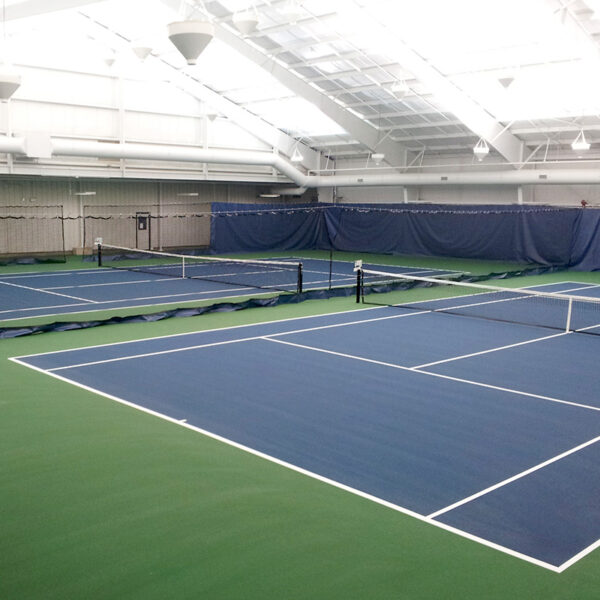 Indoor tennis facility with blue courts, white lines, nets, and green surrounding flooring