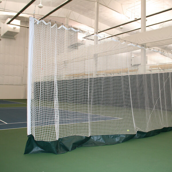 Indoor sports facility with a white net enclosure around a court or practice area; padded base along the bottom of the netting.
